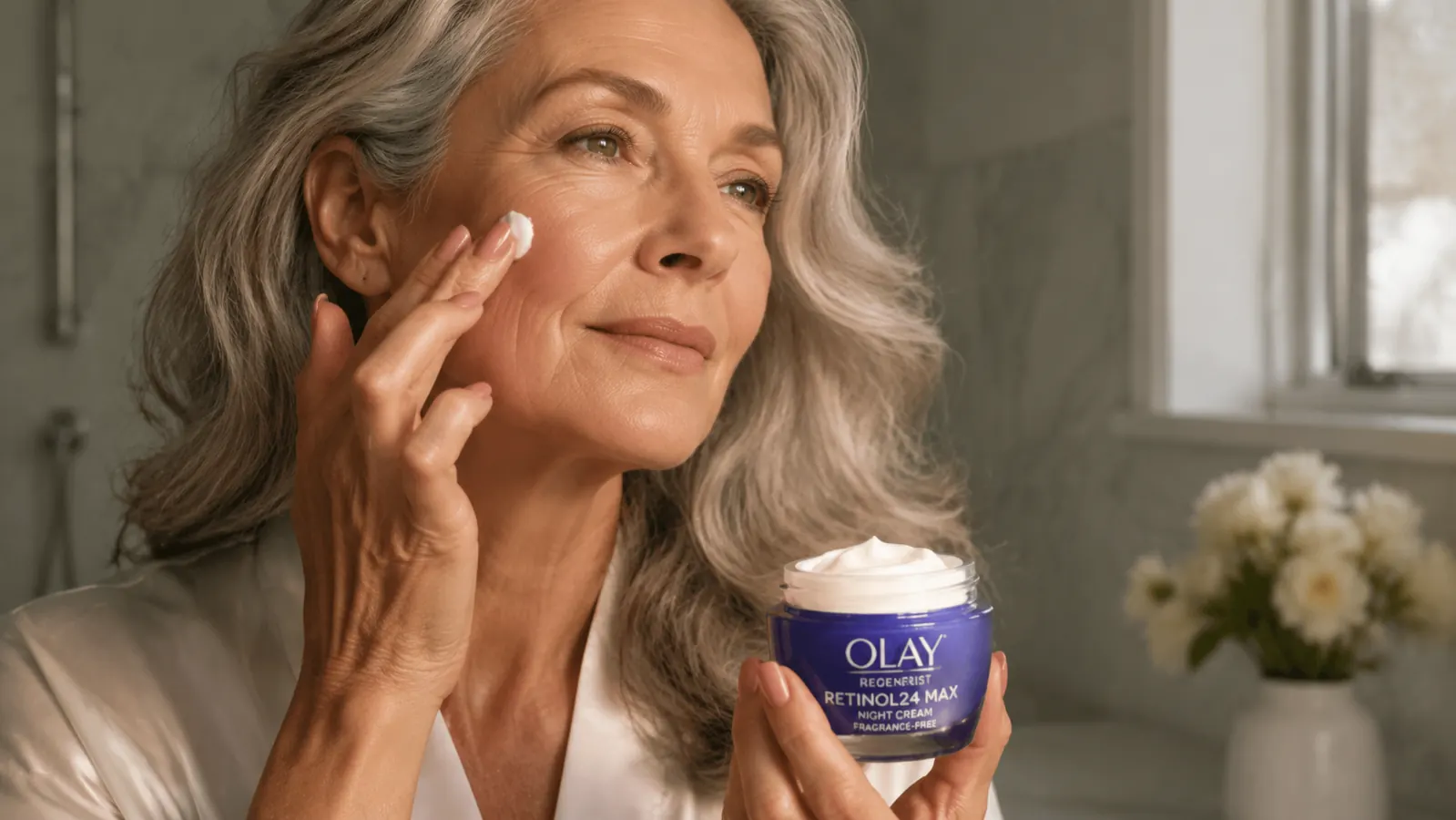 Olay Retinol Night Cream jar open on a marble bathroom counter next to a small bowl of water and a clean cotton pad