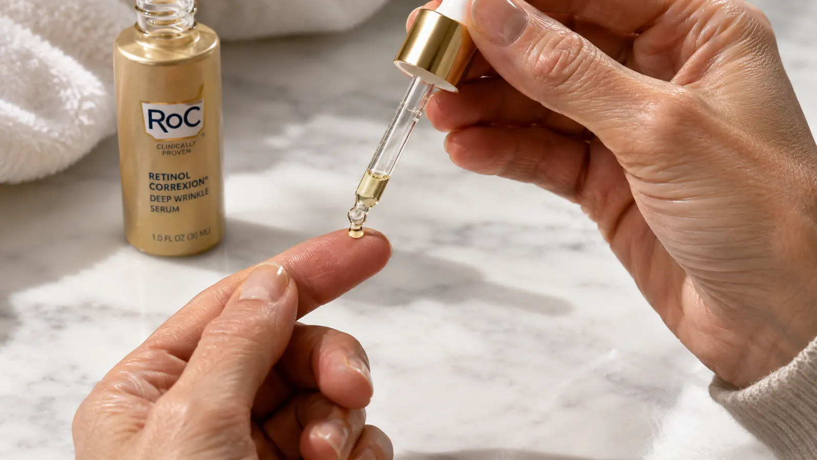 Small amount of retinol serum being dispensed from a dropper onto a fingertip, white countertop background