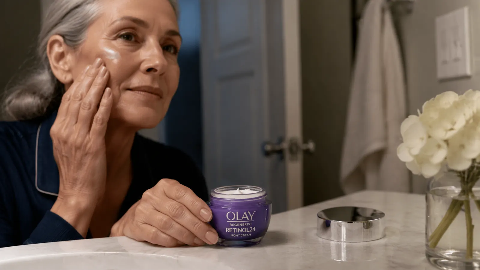 Close-up of a jar of Olay Retinol Night Cream sitting on a marble bathroom counter next to a glass of water