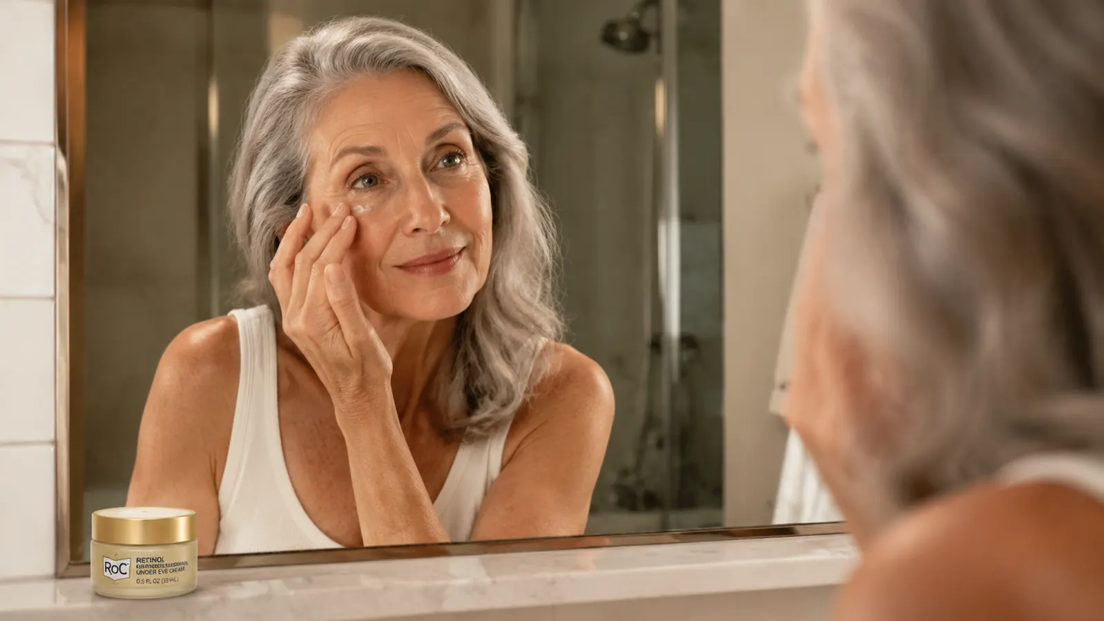 Woman in her late fifties gently applying eye cream to the under-eye area with her ring finger